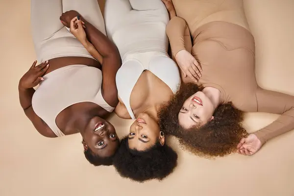 Top view of happy plus size woman in lingerie lying down on beige, natural body positive beauty — Stock Photo