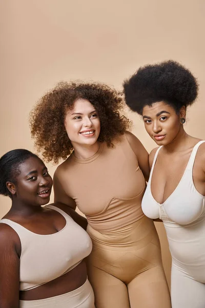 Feliz multiétnica más tamaño novias en lencería posando sobre fondo beige, belleza positiva para el cuerpo - foto de stock