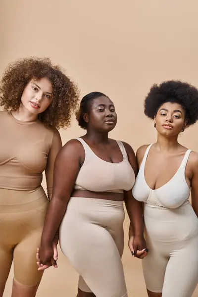 Confiantes et courbes femmes multiraciales en lingerie regardant la caméra sur beige, beauté naturelle — Photo de stock