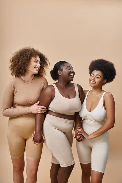 Smiling plus size multiracial women in lingerie posing on beige, beauty and body positivity — Stock Photo