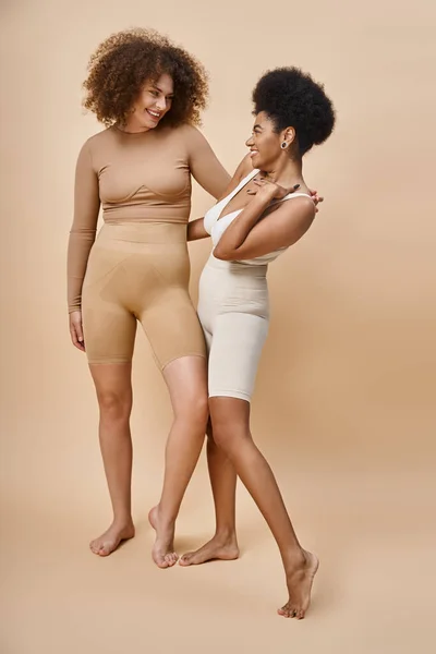 Smiling multicultural body positive women in underwear standing on beige, natural plus size beauty — Stock Photo