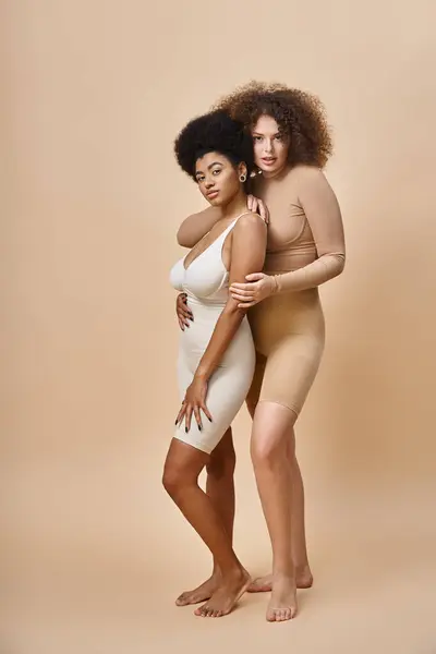 Confiante multicultural corpo positivo mulheres em roupa interior de pé em bege, natural plus size beleza — Fotografia de Stock