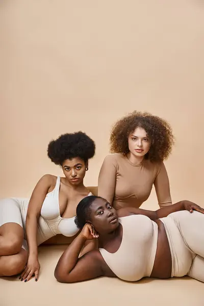 Confident multiracial plus size women in lingerie posing on beige backdrop, natural beauty — Stock Photo