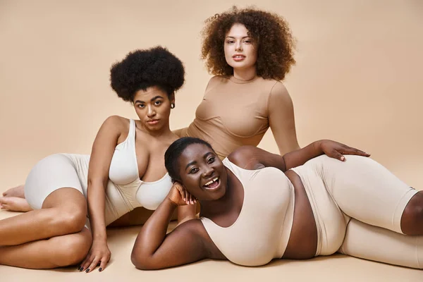 Confiant multiracial plus la taille des femmes en lingerie posant sur fond beige, beauté naturelle — Photo de stock