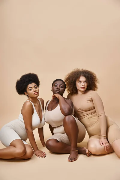 Fiducioso multirazziale plus size donne in lingerie in posa su sfondo beige, bellezza naturale — Foto stock