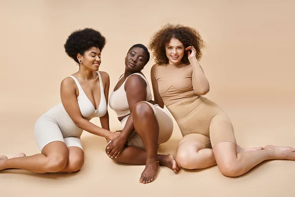 Encantadoras mulheres multirraciais em lingerie posando em pano de fundo bege, além de elegância tamanho e beleza — Fotografia de Stock