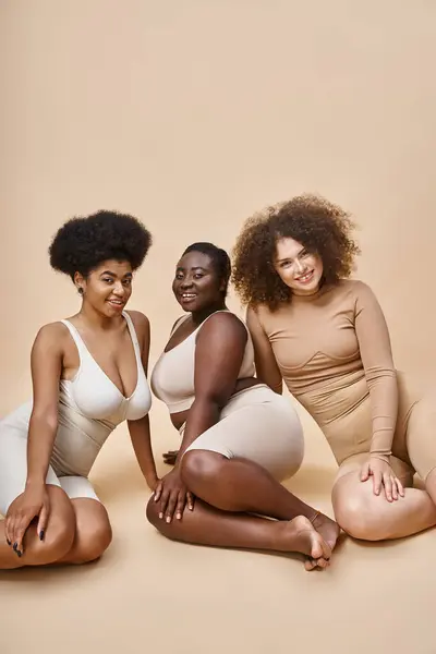Charmante multirassische Frauen in Dessous posieren auf beigem Hintergrund, plus Größe Eleganz und Schönheit — Stockfoto