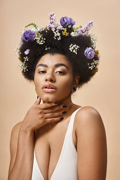 Portrait de charmante femme afro-américaine avec des fleurs colorées dans les cheveux en regardant la caméra sur beige — Photo de stock