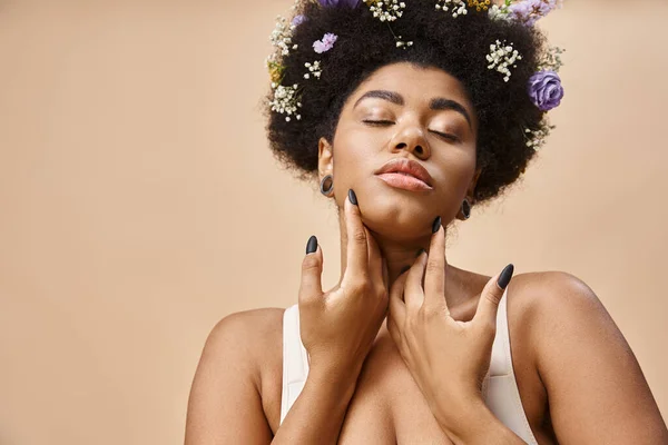 Sinnliche afrikanisch-amerikanische Frau mit bunten Blumen im Haar posiert mit geschlossenen Augen auf beige — Stockfoto