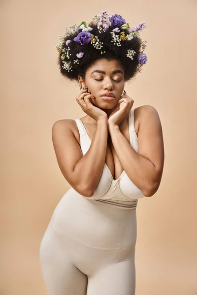 Femme africaine américaine sensuelle avec des fleurs colorées dans les cheveux posant avec les yeux fermés sur beige — Photo de stock