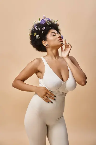 Sensual african american woman with colorful flowers in hair posing in lingerie on beige backdrop — Stock Photo