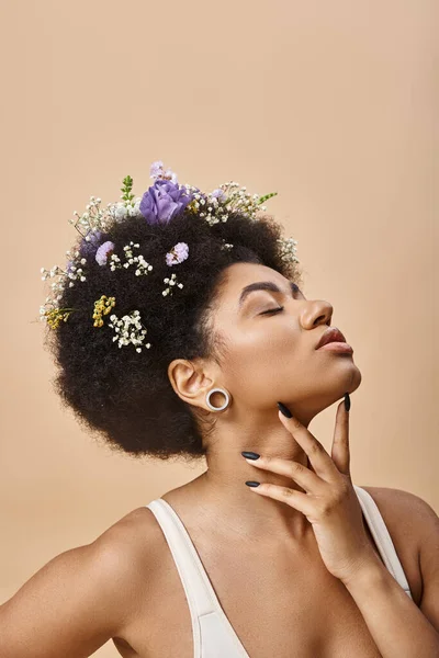 Sinnliche afrikanisch-amerikanische Frau mit bunten Blumen im Haar posiert mit geschlossenen Augen auf beige — Stockfoto