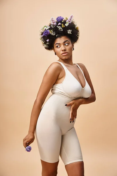 Curvy african american woman with flowers in hair posing in lingerie on beige, natural beauty — Stock Photo