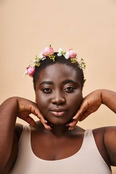 Encantador plus size mulher americana africana com flores no cabelo e mãos perto do rosto em bege — Fotografia de Stock