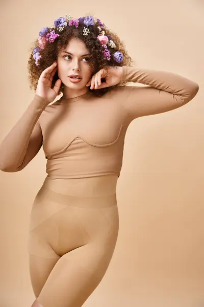 Sensual young woman in underwear posing with colorful flowers in wavy hair on beige, natural beauty — Stock Photo