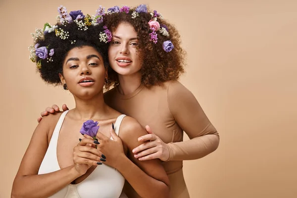 Corps multiracial femmes positives en lingerie avec des fleurs colorées dans les cheveux sur beige, plus la beauté de taille — Photo de stock