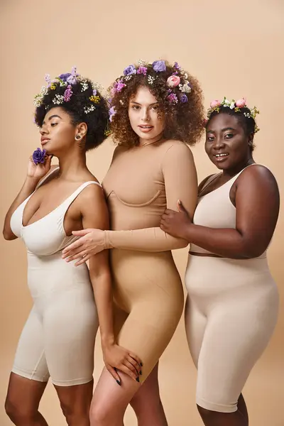 Donne multietniche plus size in lingerie con fiori colorati in capelli su beige, eleganza curvy — Foto stock