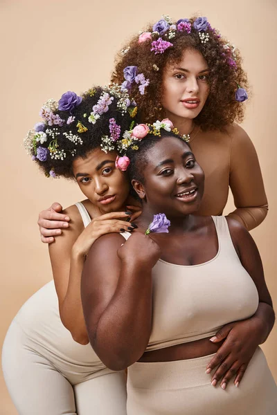 Seducente donne multirazziali in lingerie con fiori colorati in capelli su beige, plus size bellezza — Foto stock