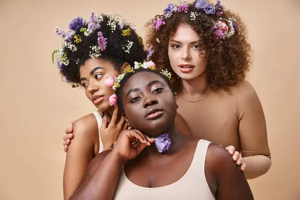 Séduisantes femmes multiraciales en lingerie avec des fleurs colorées dans les cheveux sur beige, plus la beauté de taille — Photo de stock