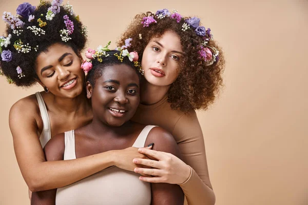 Charmantes femmes multiraciales en lingerie avec des fleurs colorées dans les cheveux sur beige, plus la beauté de taille — Photo de stock
