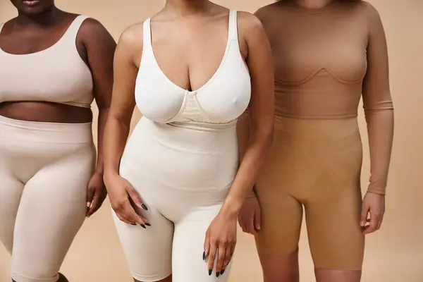 Vue recadrée de femmes multiethniques courbes en sous-vêtements debout sur fond beige, positivité du corps — Photo de stock