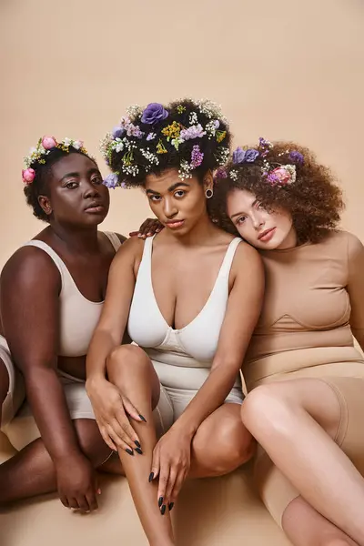 Diverse multiethnische Freundinnen in Dessous mit Blumen im Haar sitzen auf beige, plus size beauty — Stockfoto