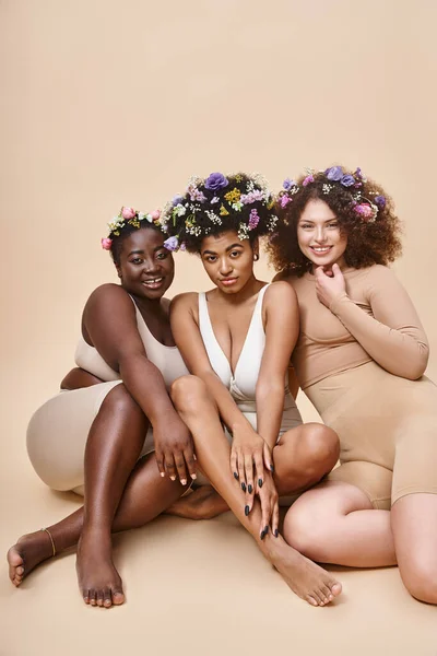 Körper positive multiethnische Frauen in Dessous mit Blumen im Haar sitzen auf beige, natürliche Schönheit — Stock Photo