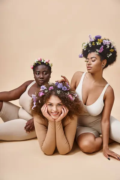 Body positive multiethnic women in lingerie with flowers in hair sitting on beige, natural beauty — Stock Photo