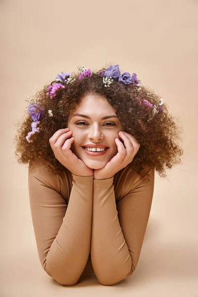 Retrato de mulher bonita e alegre com flores coloridas em cabelos ondulados em bege, beleza natural — Fotografia de Stock