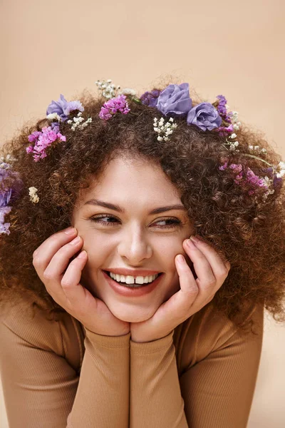 Retrato de mulher bonita e alegre com flores coloridas em cabelos ondulados em bege, beleza natural — Fotografia de Stock