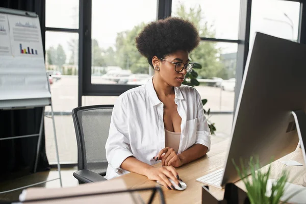 Mujer de negocios afroamericana concentrada en anteojos que trabajan en la computadora en la oficina contemporánea - foto de stock