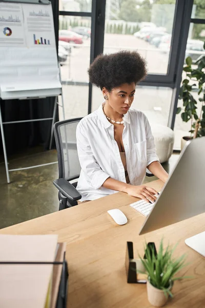 Mujer de negocios afroamericana concentrada en anteojos que trabajan en la computadora en la oficina contemporánea - foto de stock