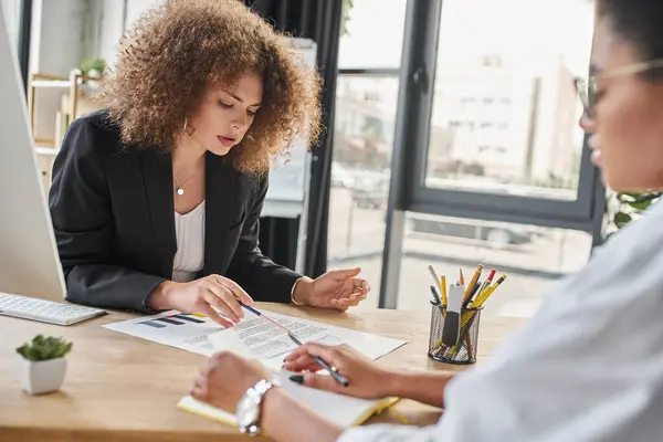 Young businesswoman working with documents near african american colleague in modern office — Stock Photo
