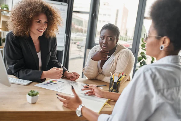 Diverse group of multiethnic businesswomen talking near documents with graphs in modern office — Stock Photo