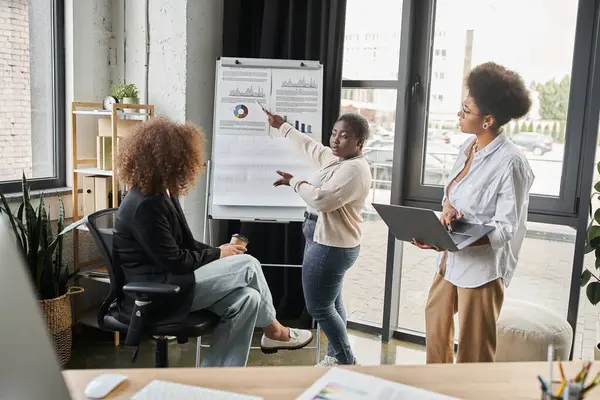 Curvilínea mulher de negócios afro-americana apontando para flip chart perto de equipe multiétnica no escritório — Fotografia de Stock