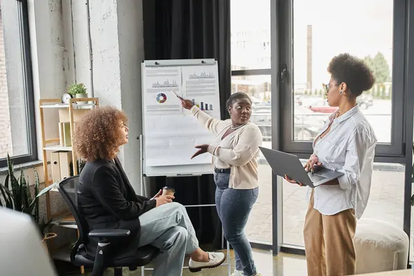 Curvy african american businesswoman pointing at flip chart near multiethnic team in office — Stock Photo