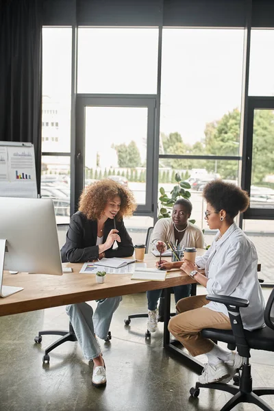 Grupo diversificado de empresárias multiculturais discutindo startup perto de laptop e documentos no escritório — Fotografia de Stock