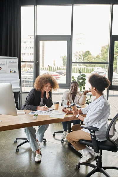 Grupo diversificado de empresárias multiculturais discutindo startup perto de laptop e documentos no escritório — Fotografia de Stock