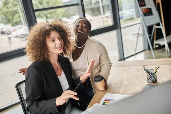 Excited interracial businesswoman talking near computer and documents in modern office, teamwork — Stock Photo