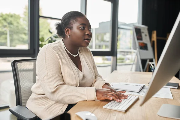 African american plus size businesswoman looking attentively on computer monitor in office — Stock Photo