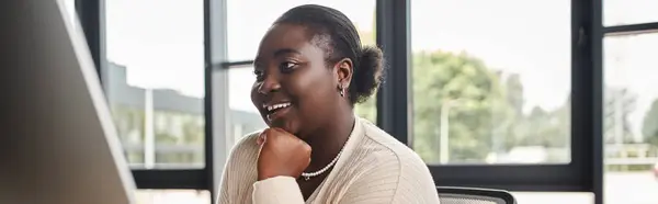 Довольный африканский американец плюс размер деловая женщина ищет на мониторе компьютера в офисе, баннер — стоковое фото