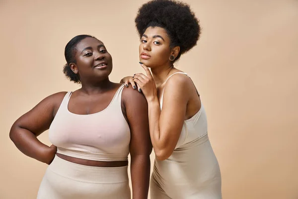 Modelos femininos afro-americanos curvilíneos em roupa interior olhando para a câmera em bege, além de beleza tamanho — Fotografia de Stock