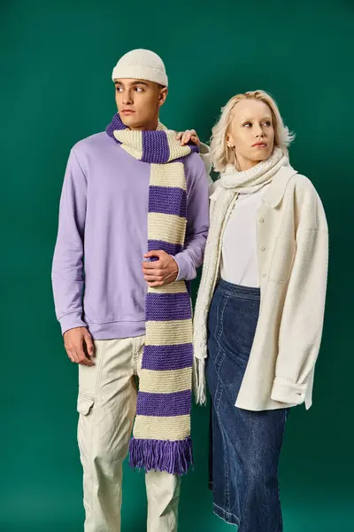 Стильная пара в зимнем наряде, блондинка позирует с мужчиной в теплой одежде на бирюзовом фоне — стоковое фото