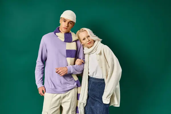 Young couple in winter attire, happy woman posing with man in stylish clothing on turquoise backdrop — Stock Photo