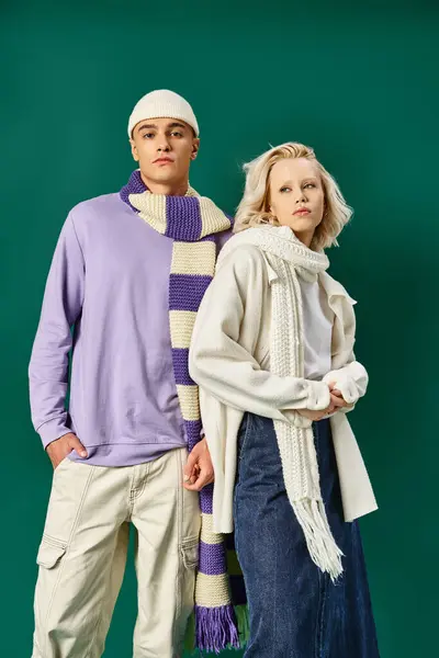 Пара в зимних нарядах, блондинка позирует с мужчиной в модной одежде на бирюзовом фоне — стоковое фото