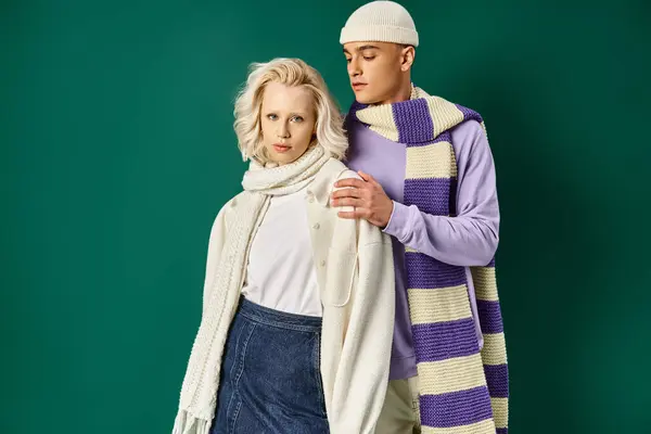 Young couple in winter attire, stylish man in putting hand on shoulder of woman on turquoise — Stock Photo