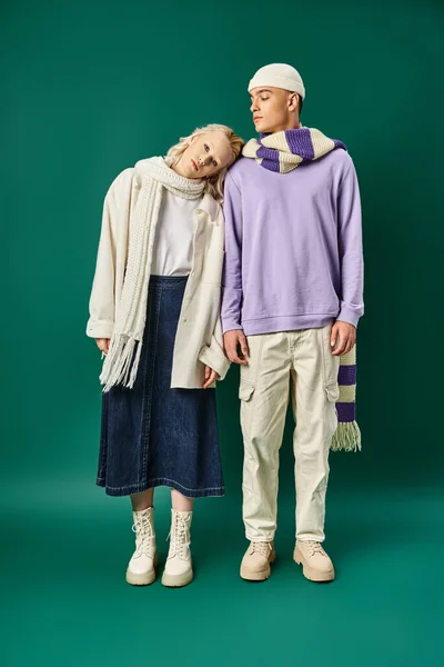 Blonde woman in stylish winter attire putting head on shoulder of tall man on turquoise backdrop — Stock Photo