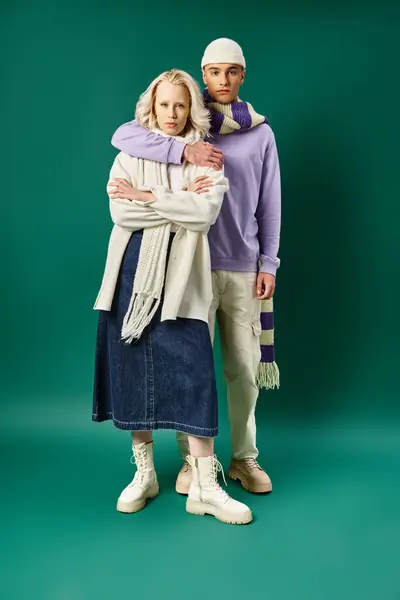 Full length of tall and stylish man hugging blonde woman in winter attire on turquoise backdrop — Stock Photo