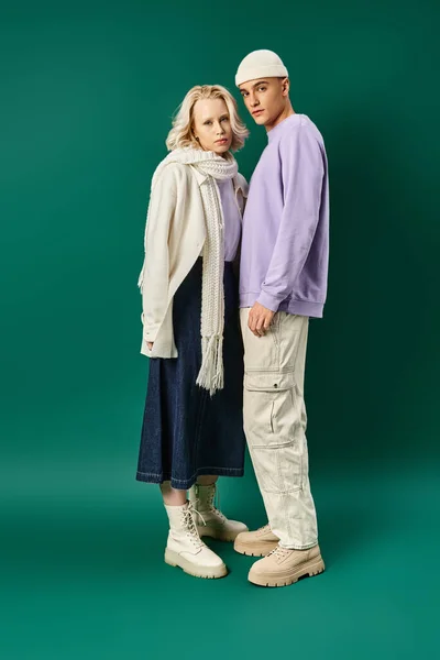 Longitud completa de hombre alto y elegante de pie con mujer rubia en traje de invierno sobre fondo turquesa - foto de stock