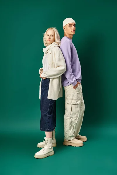 Young man in beanie hat and winter attire standing with blonde woman on turquoise backdrop — Stock Photo